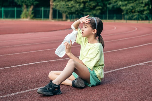 Free Photo thirsty little girl drinks water while sitting on the stadium