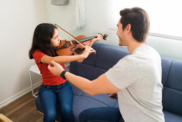 これは正しい位置です。やる気のあるプレティーンの女子生徒がバイオリンを弾くのを手伝う幸せな音楽教師