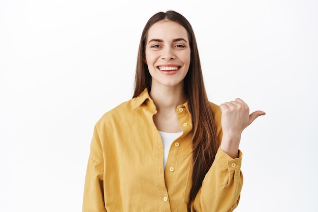 This way Smiling attractive woman with natural makeup points aside showing right copyspace making announcement show promo text standing over white background