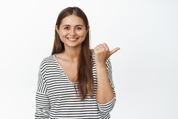 This way. smiling girl showing direction, pointing finger right and looking happy, recommending store or sale banner on white