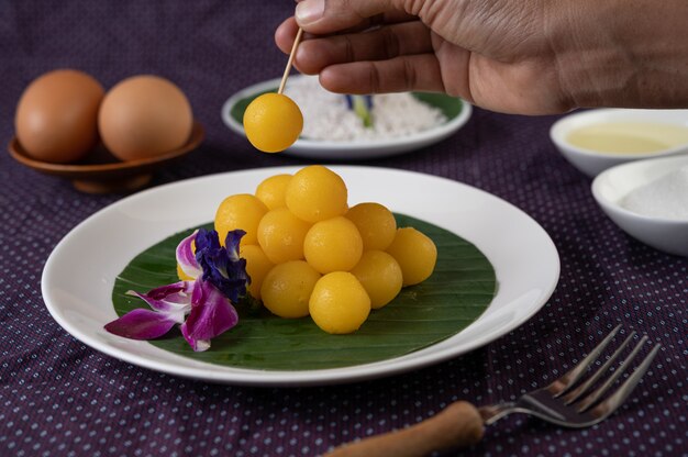 Десерт Thong Yod на банановом листе в белой тарелке с орхидеями и вилкой