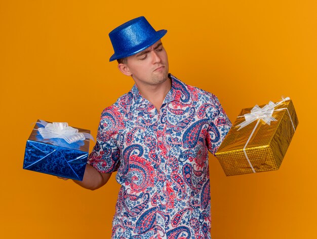 파란색 모자를 쓰고 오렌지에 고립 된 선물 상자를보고 사려 깊은 젊은 파티 남자