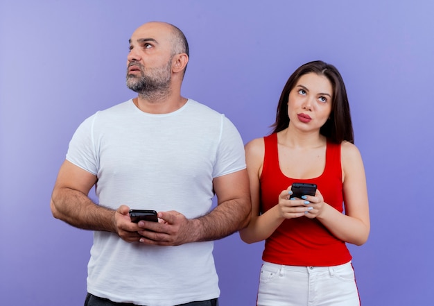 Thoughtful adult couple both holding mobile phones man looking at side and woman looking up 