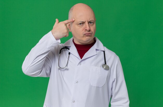 Вдумчивый взрослый мужчина в униформе врача со стетоскопом, положив палец на висок и глядя