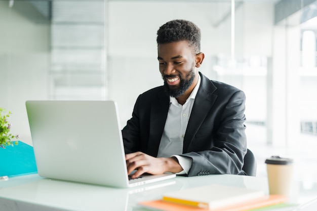 Вдумчивый афро-американский бизнесмен, используя ноутбук, обдумывая проект, бизнес-стратегию, озадаченный руководитель работника, глядя на экран ноутбука, чтение электронной почты, принятие решения в офисе