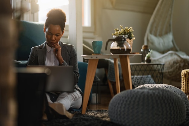 Free photo thoughtful african american businesswoman working on a computer while siting on the floor at home office