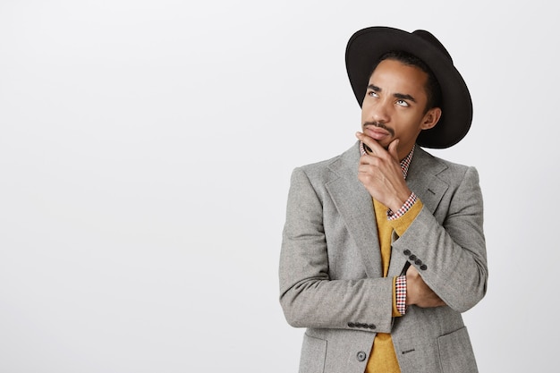 Thoughtful african-american man in suit making decision, touching chin and look upper left corner, pondering choice