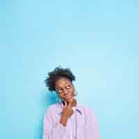 Free photo thoughtful african american woman holds chin looks above makes decision ponders on