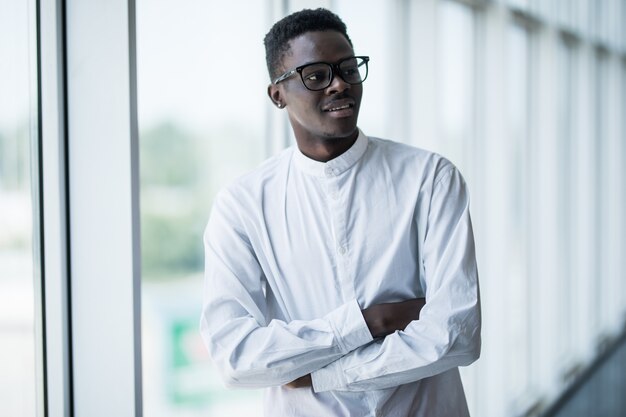 Thoughtful african businessman with arms crossed in office against panoramic window