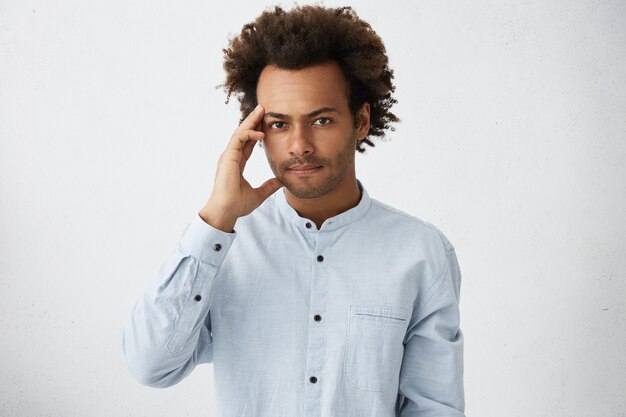 Thoughtful Afro American businessman in formal clothes having fluffy dark hair holding hand on temple