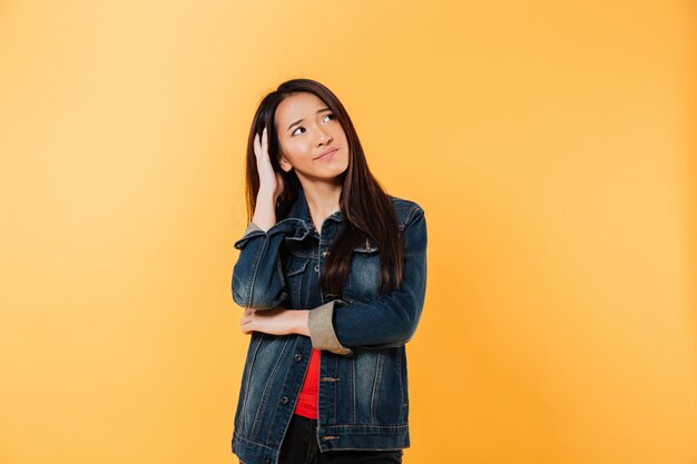 Thoughtful asian woman in jacket holding head and looking away