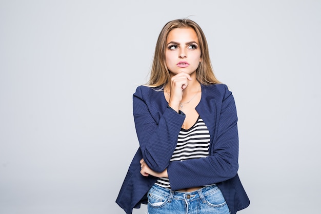 Giovane donna attraente premurosa che pensa e che distoglie lo sguardo sopra un muro bianco