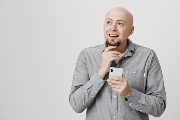 Thoughtful bald adult man thinking as order food online with smartphone app