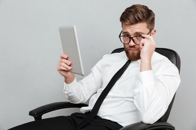 Thoughtful bearded busienssman holding pc tablet and looking over eyeglasses