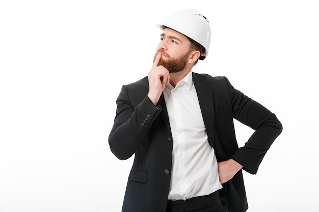 Thoughtful bearded business man in protective helmet looking away