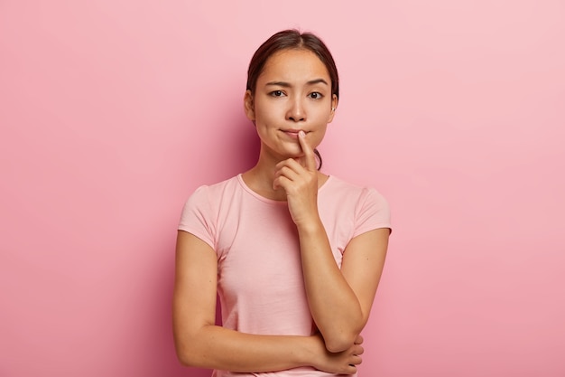 La bella ragazza asiatica premurosa pensa a qualcosa, prende decisioni, medita sulle azioni future, vestita con abiti casual, ha un aspetto specifico