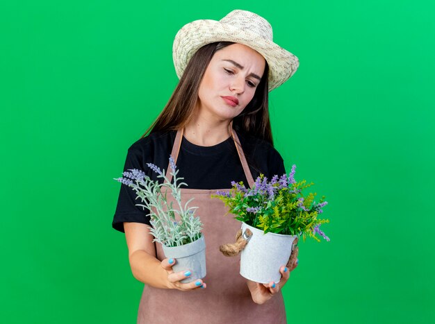 緑で隔離植木鉢の花を保持し、見てガーデニング帽子を身に着けている制服を着た思いやりのある美しい庭師の女の子