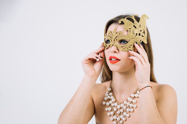 金色の装飾的なカーニバルマスクとネックレスを着て思いやりのある美しい女性