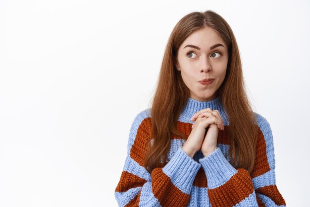 Thoughtful beauty girl, look pensive aside, reading promotional text and thinking, having interesting idea, standing in sweater over white background