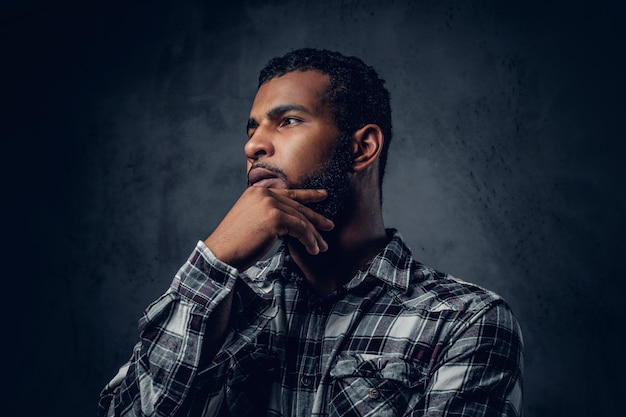 Thoughtful Black, bearded male with crossed arms over grey background.