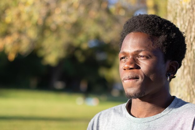 Вдумчивый черный парень проводит время на свежем воздухе в городском парке. Портрет красивого афроамериканца в серой футболке, смотрящего в сторону и думающего. Выстрел крупным планом. Молодежь, образ жизни, концепция досуга.