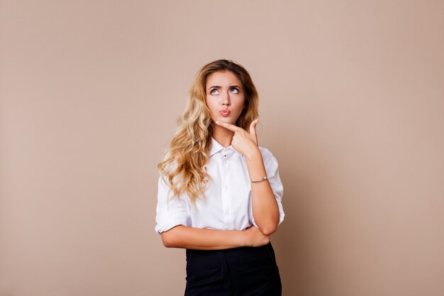 Thoughtful blond woman posing isolate on beige wall. Stylish casual workwear.