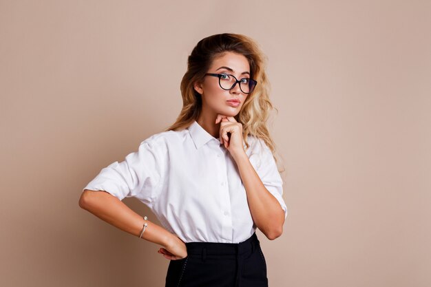 Thoughtful blond woman posing isolate on beige wall. Stylish casual workwear.