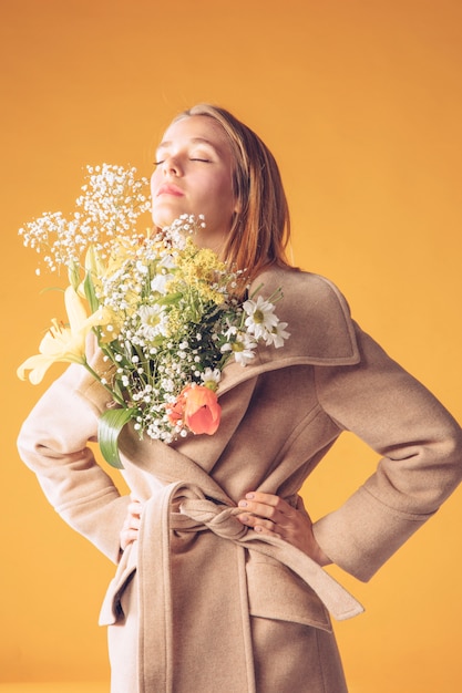 Donna bionda premurosa con bouquet di fiori in cappotto