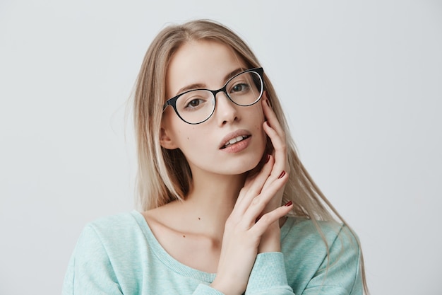 Thoughtful blonde female with attractive appearance in light blue sweater wearing stylish spectacles