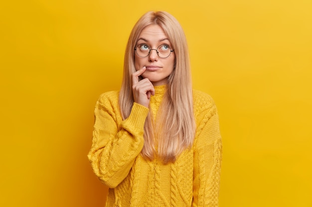 thoughtful blonde woman concentrated above being deep in thoughts wears round spectacles casual jumper 