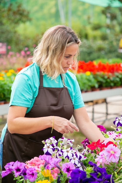 鉢植えの花の植物を見ている思いやりのある金髪の女性