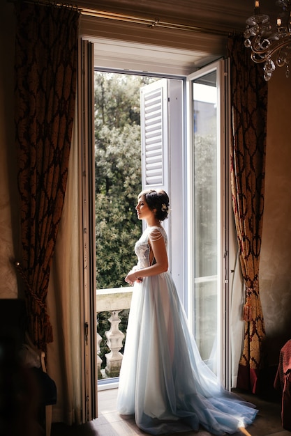 Thoughtful bride stands before an open window in the morning