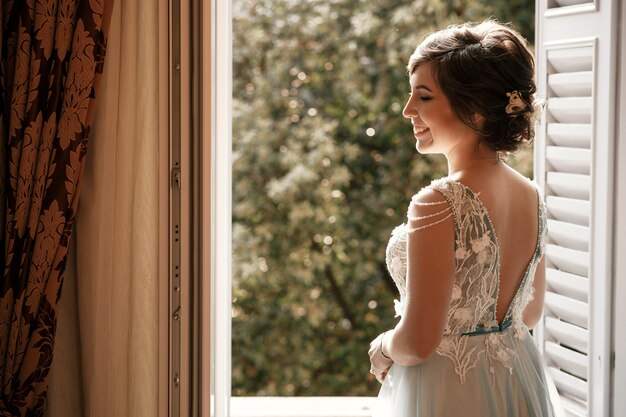 Thoughtful bride stands before an open window in the morning