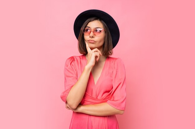 Thoughtful brunette woman in stylish glasses posing over pink wall.