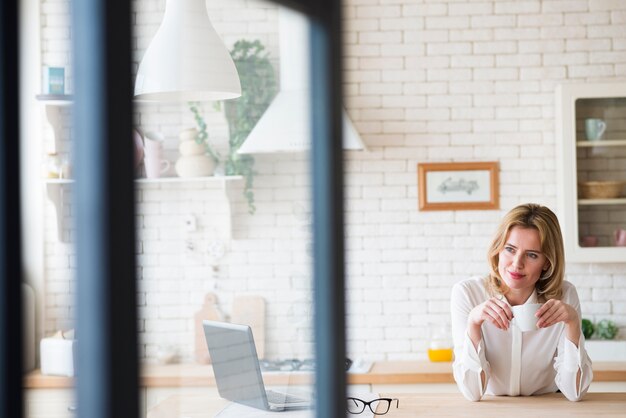 Foto gratuita donna premurosa di affari che si siede con la tazza e il computer portatile di caffè