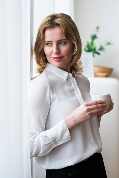 Thoughtful business woman standing with coffee cup