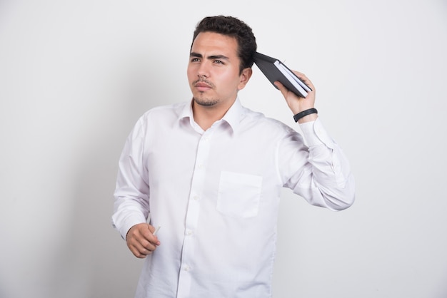 Thoughtful businessman with notebook standing on white background.