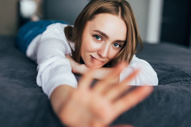 Thoughtful casual brown haired woman in white pajamas lying on her bed in a bright bedroom