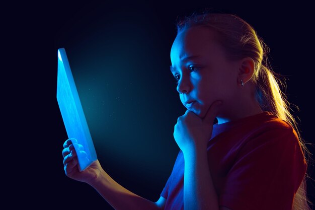 인정 있는. 네온 불빛에 어두운 스튜디오 배경에 백인 여자의 초상화. 태블릿을 사용하는 아름다운 여성 모델.