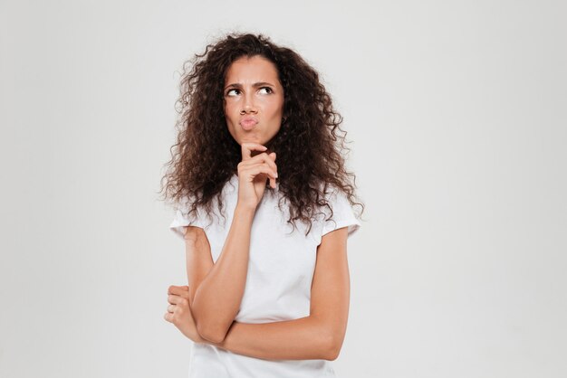 Thoughtful curly woman holding hand on chin and looking away