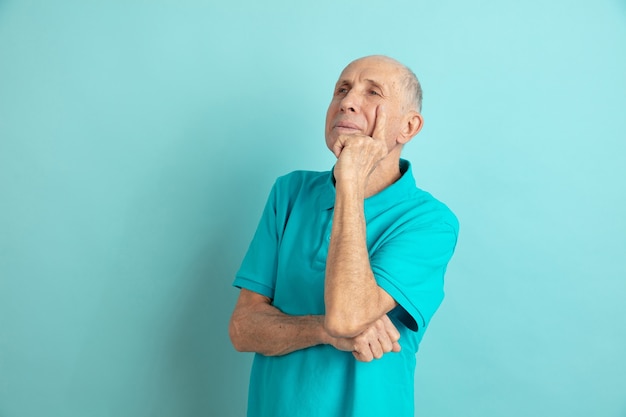 Thoughtful, dreaming. Caucasian senior man's portrait on blue studio.