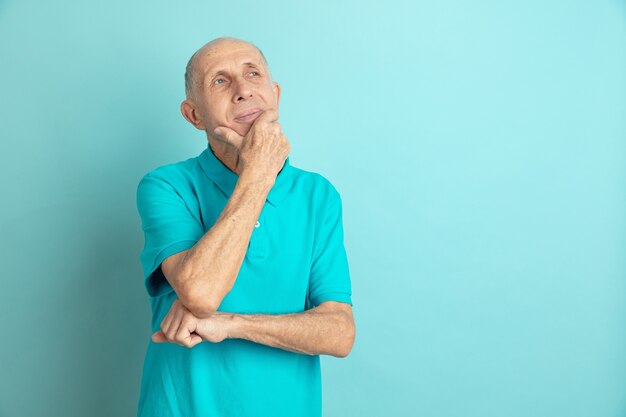 Задумчивый, мечтательный. Портрет кавказского старшего человека, изолированные на синем фоне студии. Красивая мужская эмоциональная модель. Понятие человеческих эмоций, выражения лица, продаж, благополучия, рекламы. Copyspace.