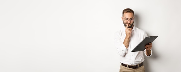 Free photo thoughtful employee looking at clipboard having doubts standing over white background