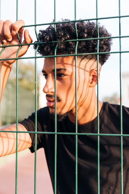 Free photo thoughtful ethnic young man behind fence