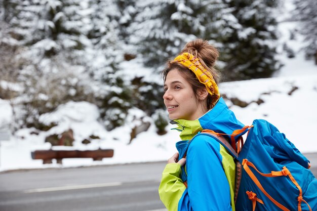Thoughtful European woman focused aside, strolls and treks near snowy mountains in winter, enjoys landscape