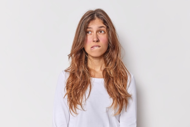 Free photo thoughtful european woman with long hait bites lips considers something has pensive expression dressed in casual jumper isolated over white background makes plan in mind searches for solution