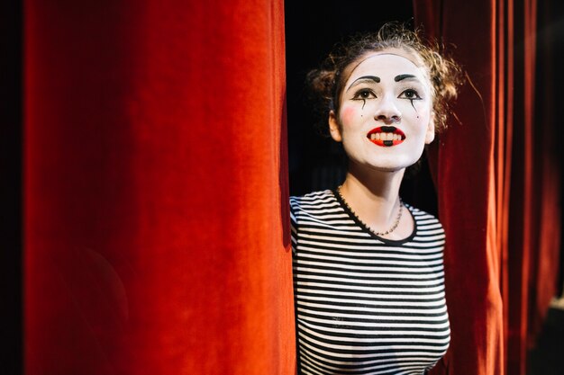 Thoughtful female mime artist standing near red curtain