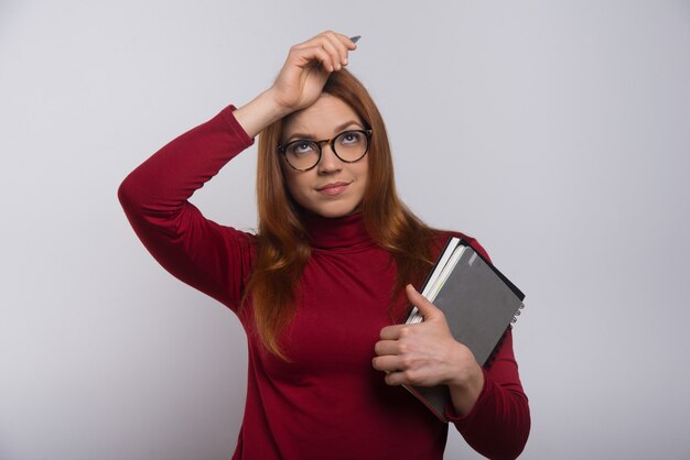 Thoughtful female student with textbooks and pen