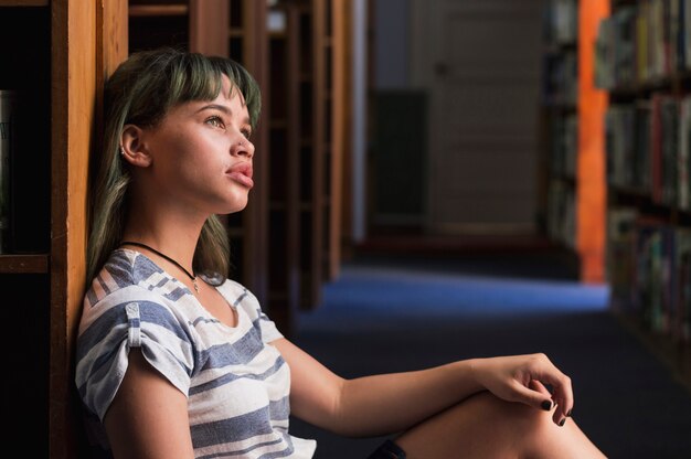 Thoughtful girl leaning against a bookshelf