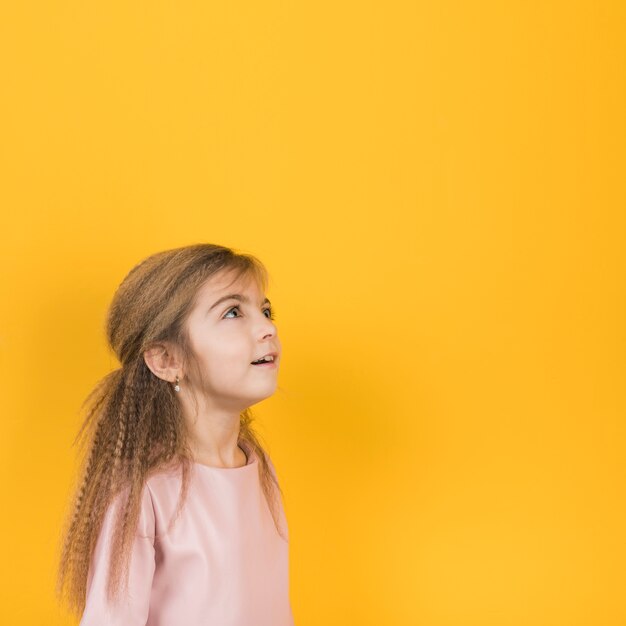 Thoughtful girl looking up on yellow background 